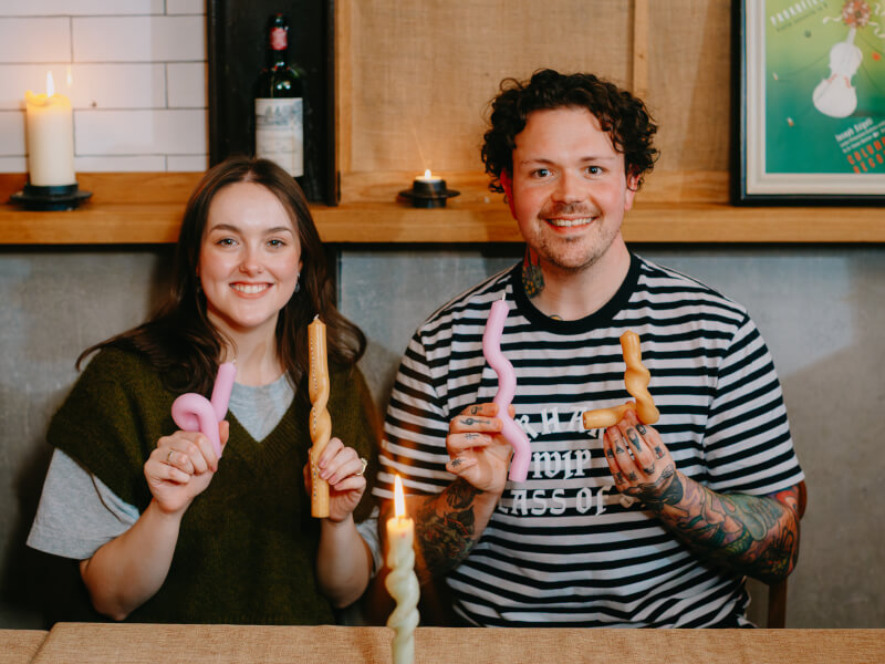 A man and woman sit at a table holding bendy candles they've made and painted
